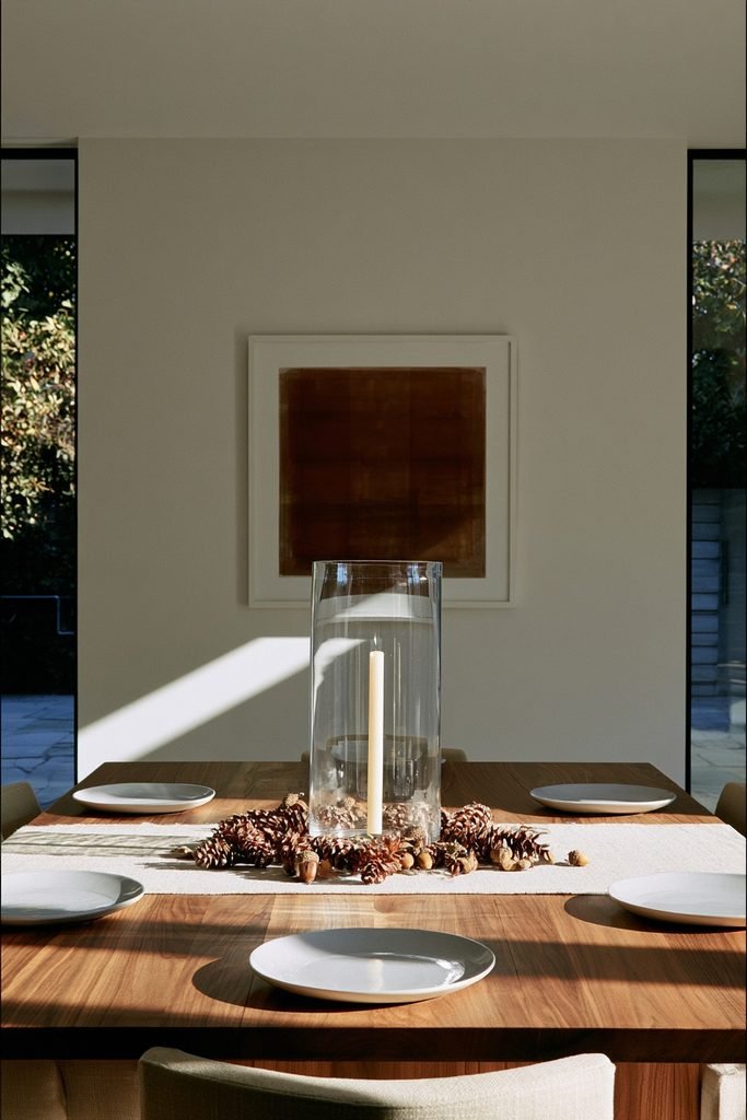 Clear glass hurricane candle holder with pinecones and acorns on a fall dining table