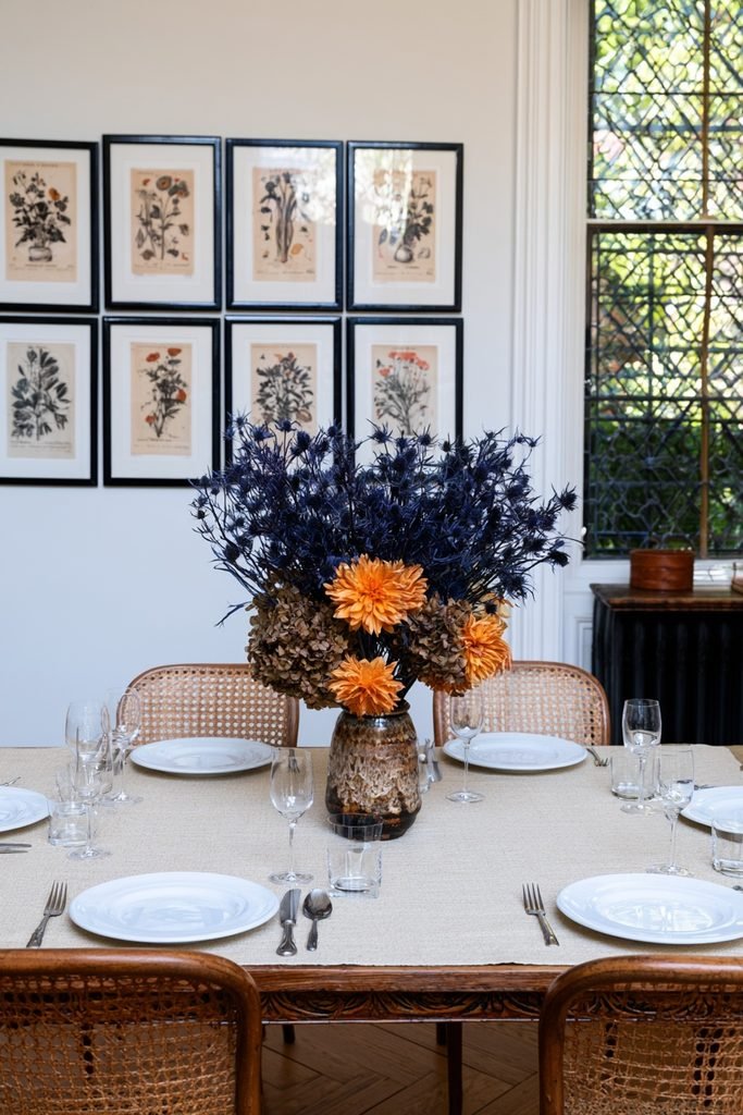 Orange dahlias and blue thistles arranged together in a fall floral centerpiece