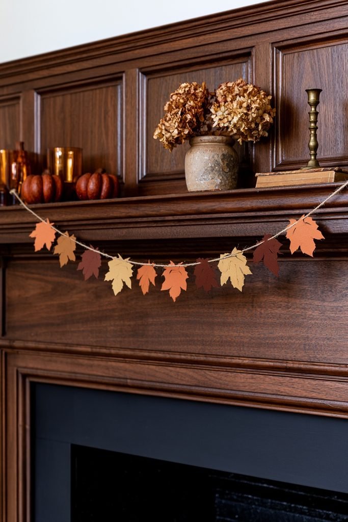 Scandinavian minimalist fireplace with a burnt orange and mustard cardstock leaf garland, neutral pumpkins, and pampas grass.