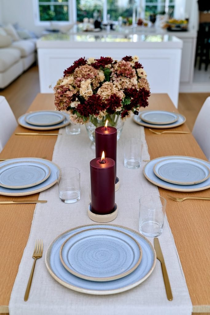 Rust and burgundy pillar candles in neutral glass holders on a fall table
