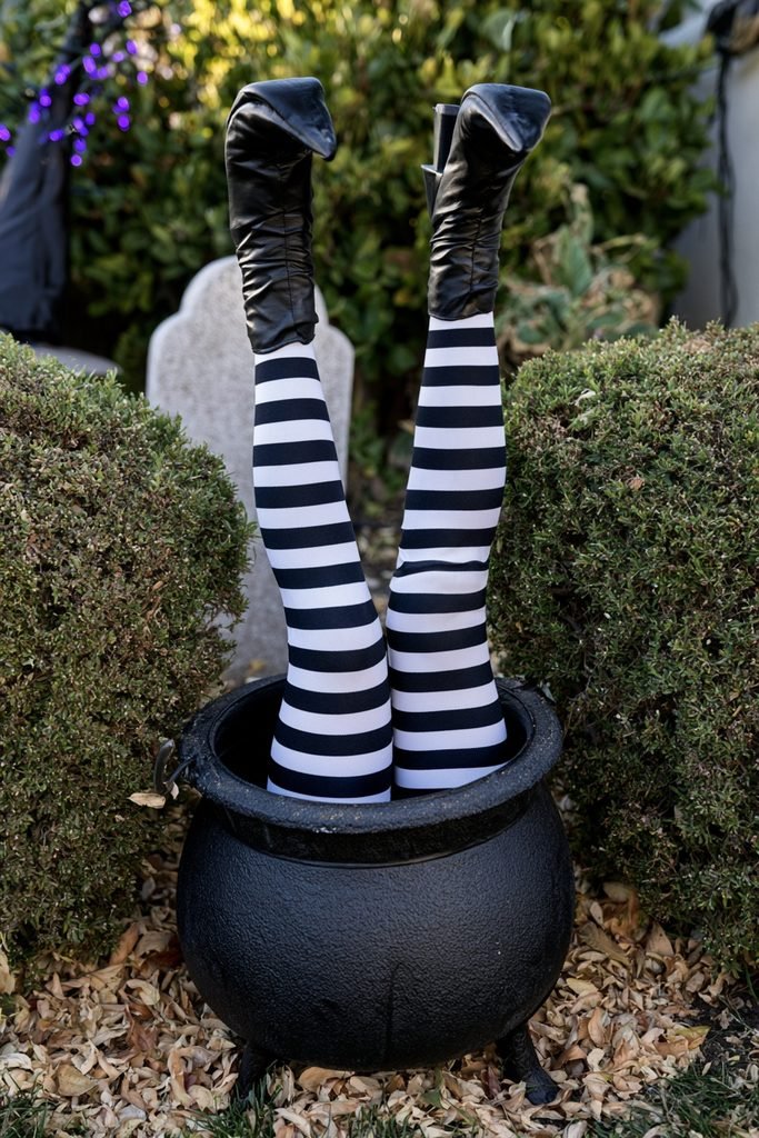 Striped witch legs and black boots sticking out of a Halloween cauldron in the yard.