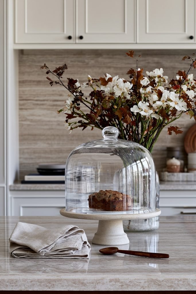 Glass cake dome with pumpkin muffins on a walnut pedestal in a modern dark kitchen