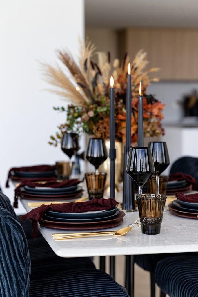 Dramatic jewel-tone fall dining table decor with plum, burgundy and deep teal accents, gold cutlery and an autumn centerpiece.