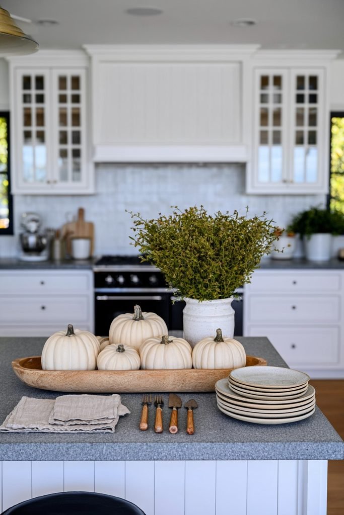 Low rustic dough bowl filled with faux pumpkins and greenery decorating a fall kitchen island.