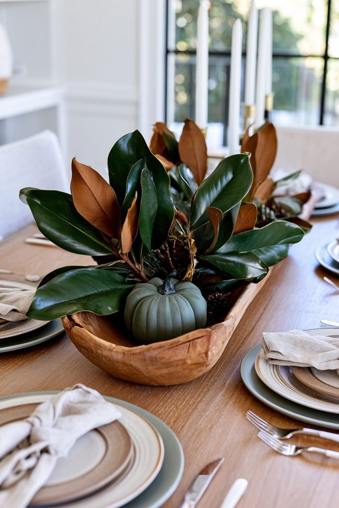 Wooden dough bowl decorated with deep green magnolia leaves and a small green pumpkin for fall.