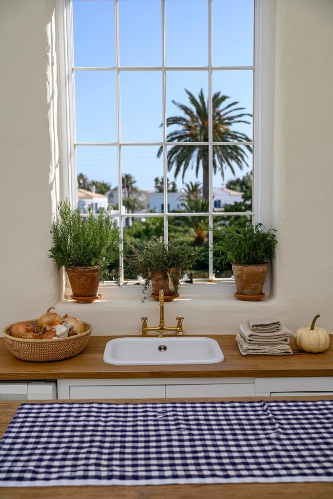 Terracotta pots of rosemary, thyme, and sage on a modern kitchen windowsill