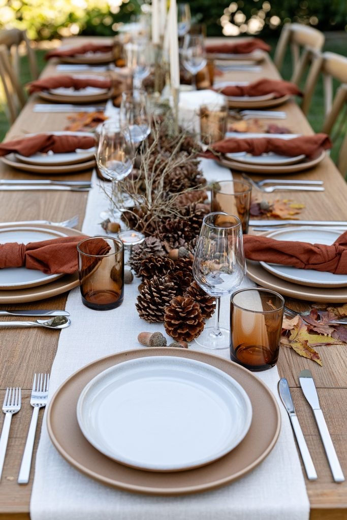 Natural fall dining table decor with pinecones, acorns, twigs, autumn leaves and warm seasonal place settings.