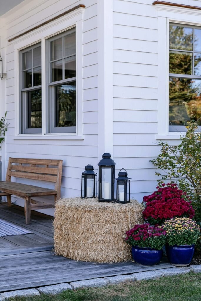 Farmhouse fall porch corner vignette with a hay bale, lanterns, and potted mums
