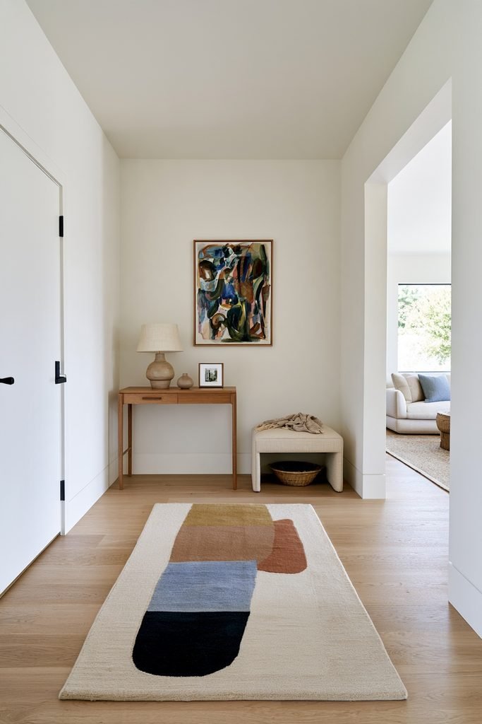 Abstract art-inspired hallway runner in a modern home with an offset entry door, oak console, colorful artwork, bench, and living room opening.