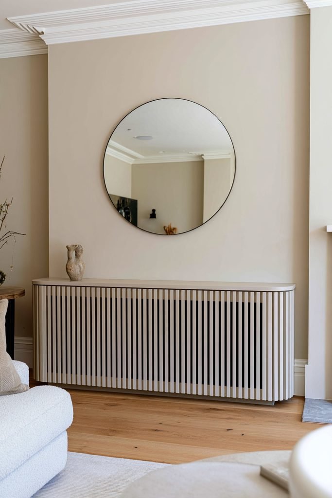 Fluted greige radiator cover with vertical grooves beneath a wall mirror