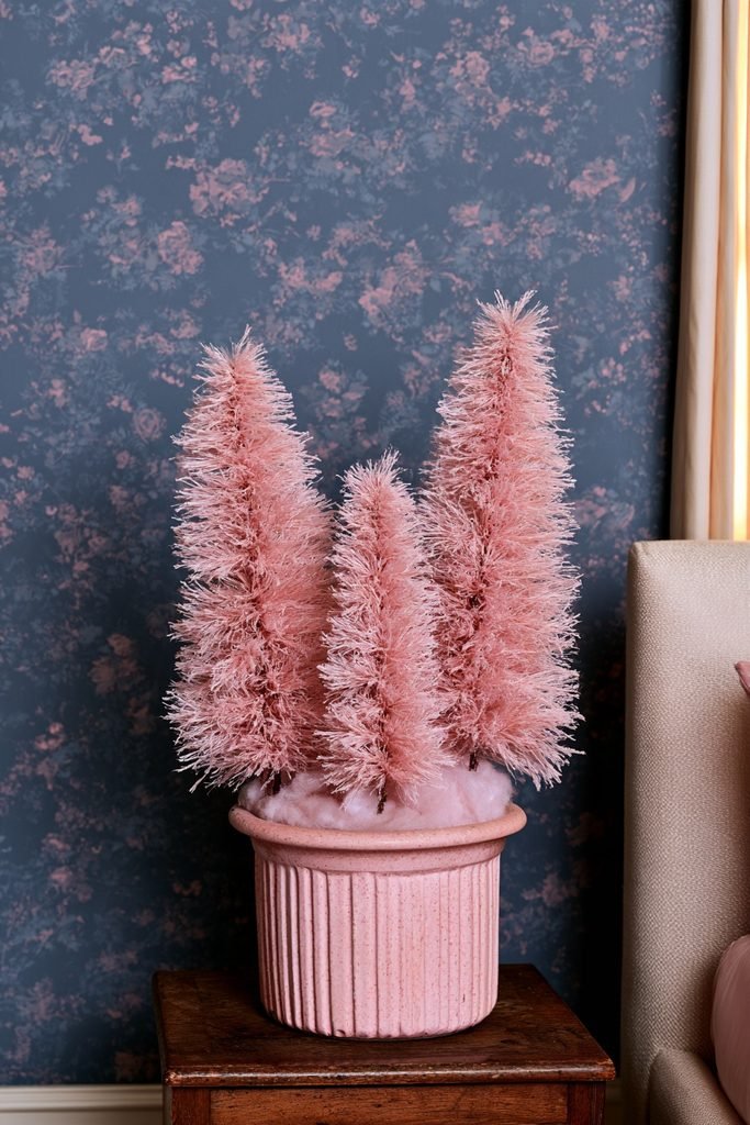 Antique vintage planter holding three small pink bottlebrush Christmas trees in a bedroom