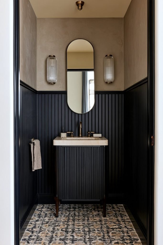 Black beadboard wainscoting in a sophisticated powder room with brass fixtures, warm lighting and contrasting neutral surfaces