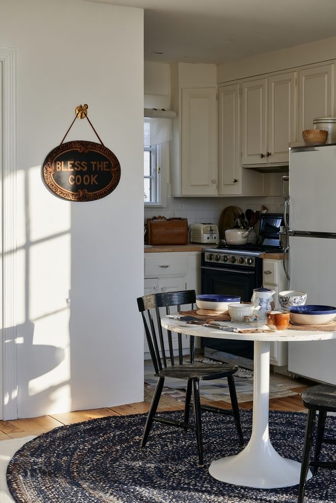 Vintage oval "Bless the Cook" kitchen sign hanging beside a cozy cottage kitchen dining area.