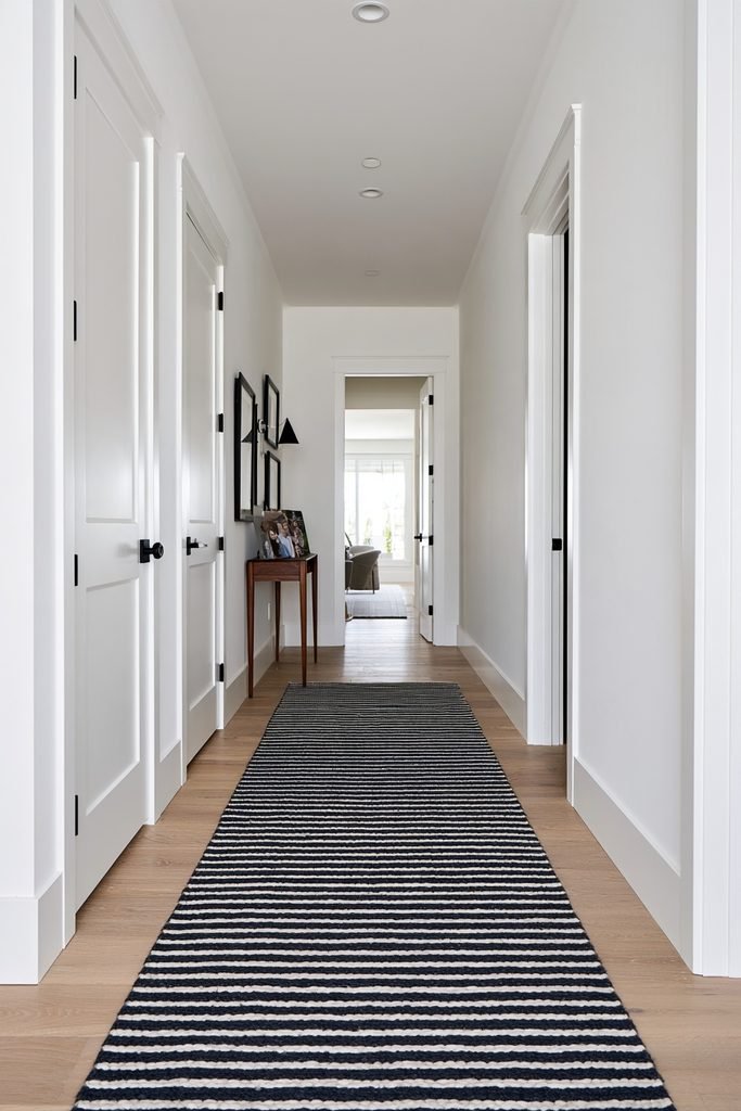 Bold striped hallway runner in a narrow sage-green home hallway with framed artwork, wood flooring, and a small window.