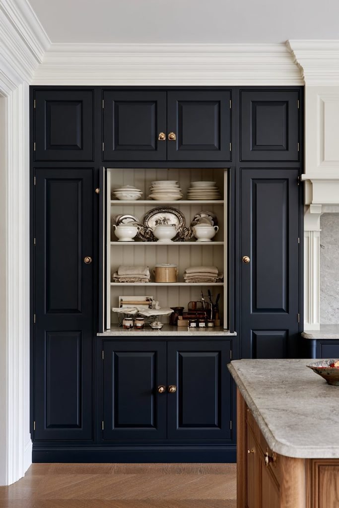 Georgian-style larder cupboard with symmetrical paneled doors, antique brass hardware, timber shelves, and organized storage