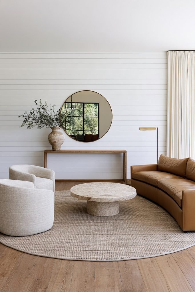 White horizontal shiplap feature wall in a cozy transitional living room with a caramel leather sofa, marble coffee table, and neutral decor.