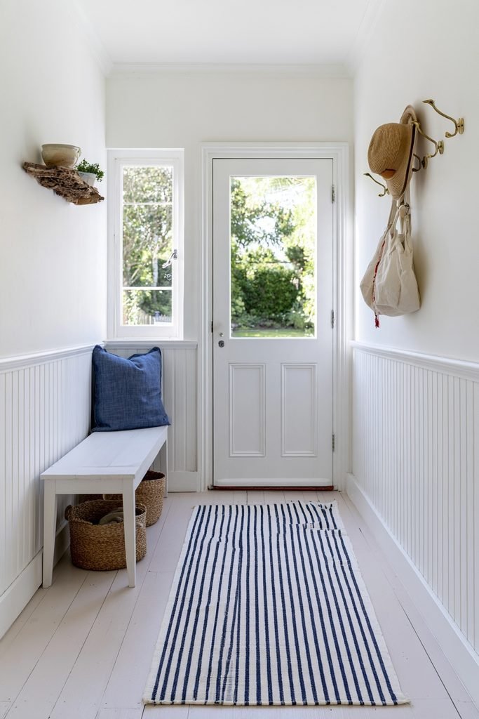 Blue and white coastal striped hallway runner in a bright cottage entry with beadboard walls, pale wood floors, bench, windows, and baskets.