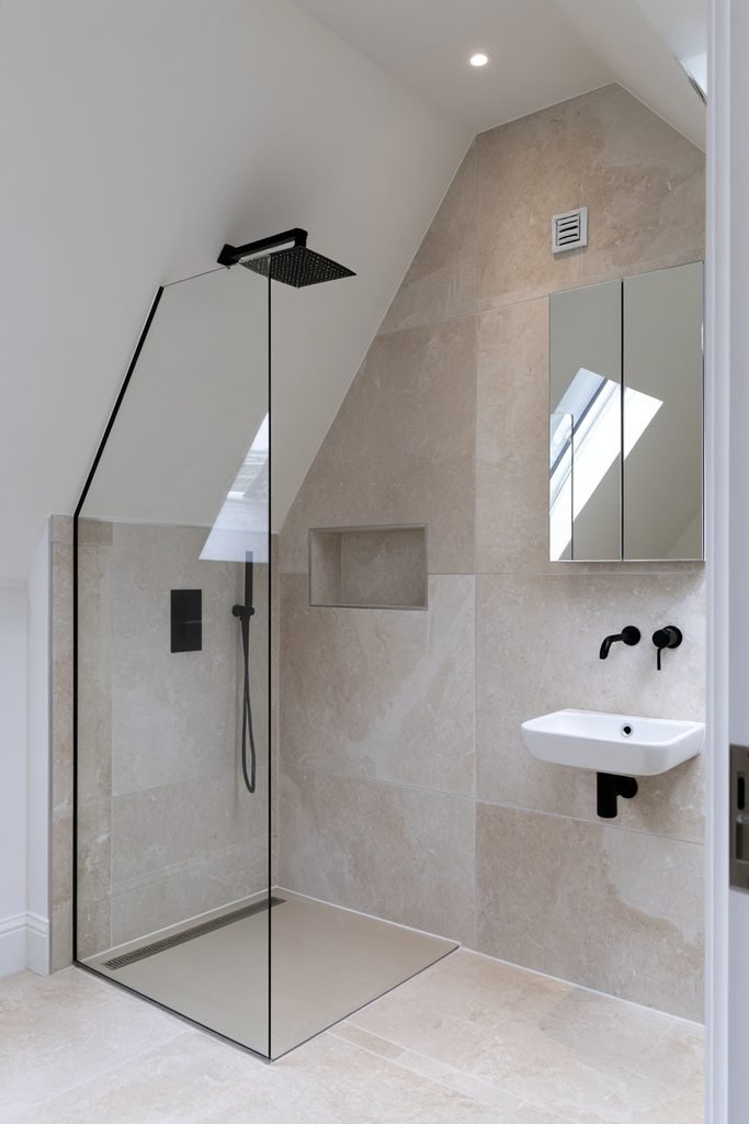 Small loft shower room with pitched roof, compact walk-in shower, wall-hung toilet, rooflight, and large-format tiles