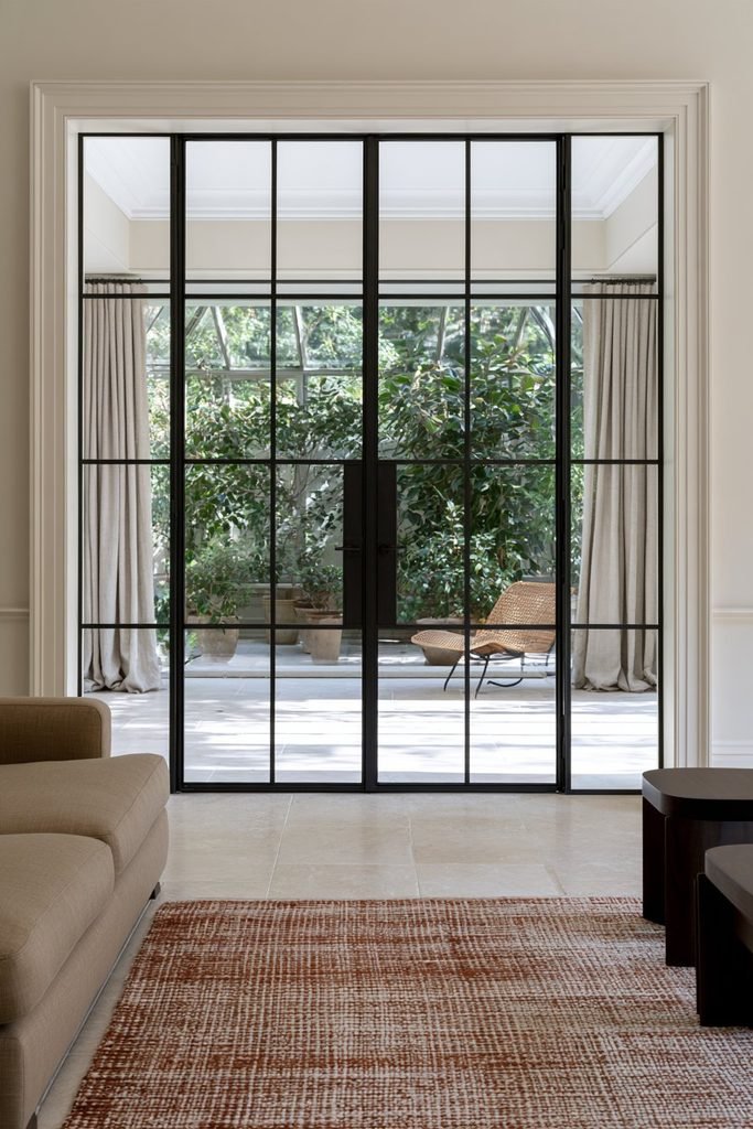 Traditional home with charcoal Crittall glass doors connecting the living room to a bright conservatory