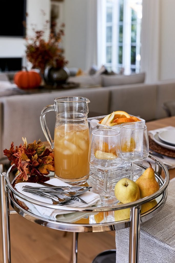 Thanksgiving drinks station on a modern bar cart with a seasonal spiced pear drink, glassware, and garnishes.