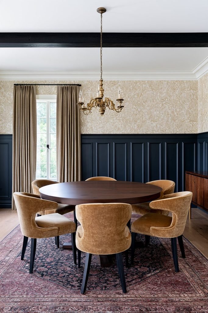 Deep navy wainscoting with patterned wallpaper in an elegant dining room featuring a wood dining table and classic lighting