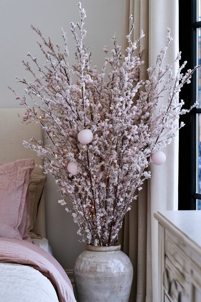 Flocked blush pink Christmas branches arranged in a vase in a cozy holiday bedroom corner