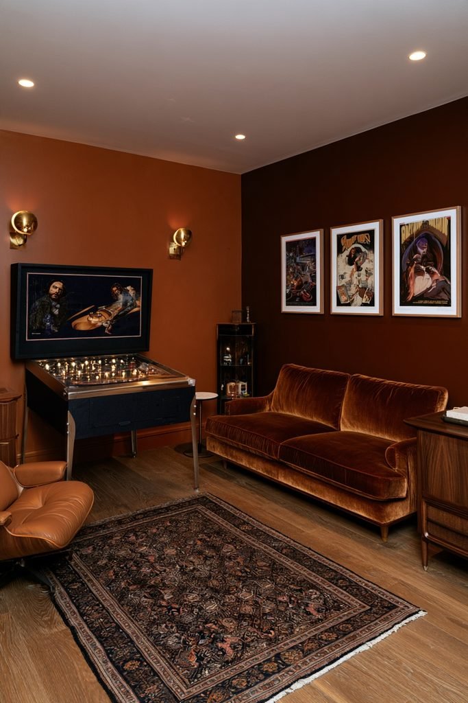 Modern basement game room featuring a stylish pinball machine, arcade cabinet, gaming sofa, collectible displays, acoustic panels, and LED lighting.
