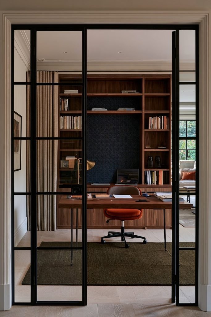 Modern home office enclosed by black Crittall glass doors with a walnut desk and built-in storage
