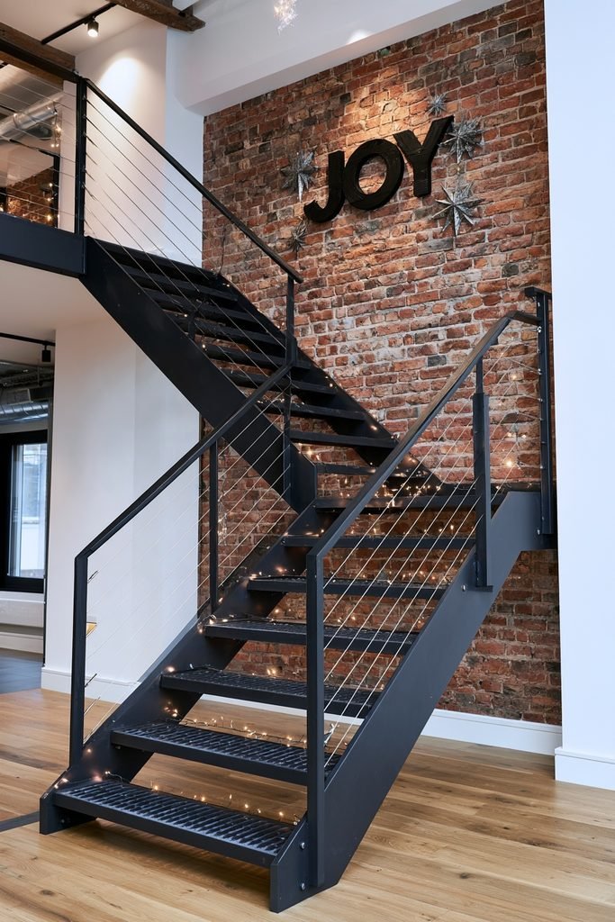 Industrial metal staircase with warm Christmas lights and a large JOY sign in a festive loft interior.