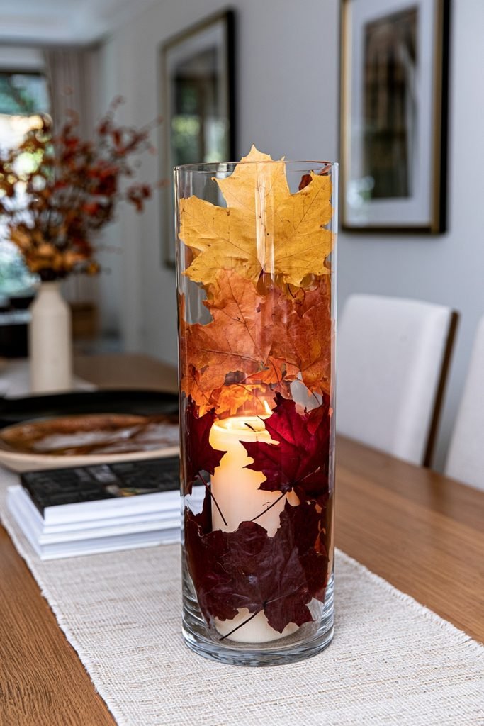 Ombré fall leaf candle jars with red orange and yellow leaves arranged on a dining room sideboard.