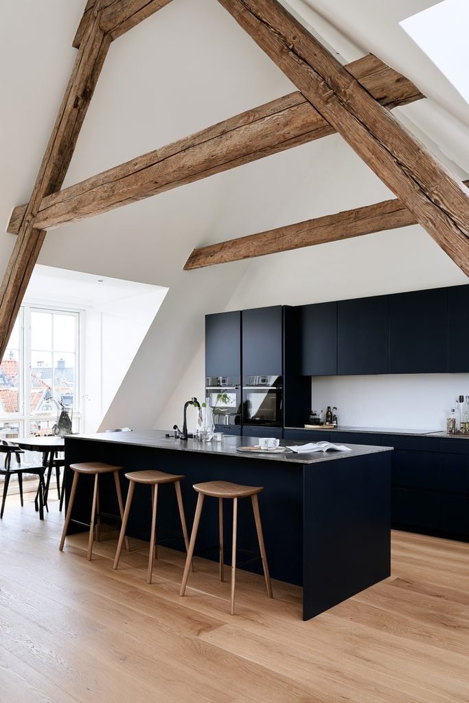 Compact loft kitchen with sloped roof, dark cabinetry, small peninsula, timber beams, and natural oak flooring