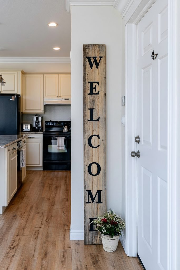 Tall vertical "Welcome" wooden sign leaning beside a kitchen entry door with flowers.