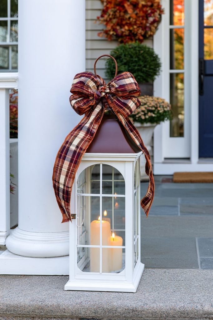Fall porch lantern decorated with warm plaid ribbon in a realistic autumn entryway