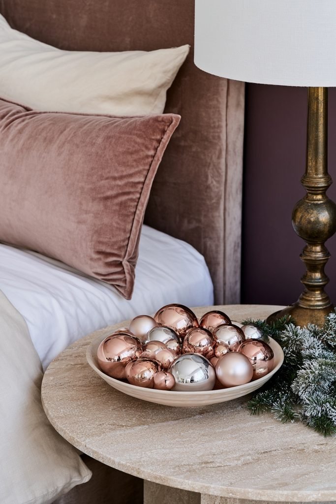 Glossy pink and silver Christmas ornaments arranged in a decorative bowl in a bedroom