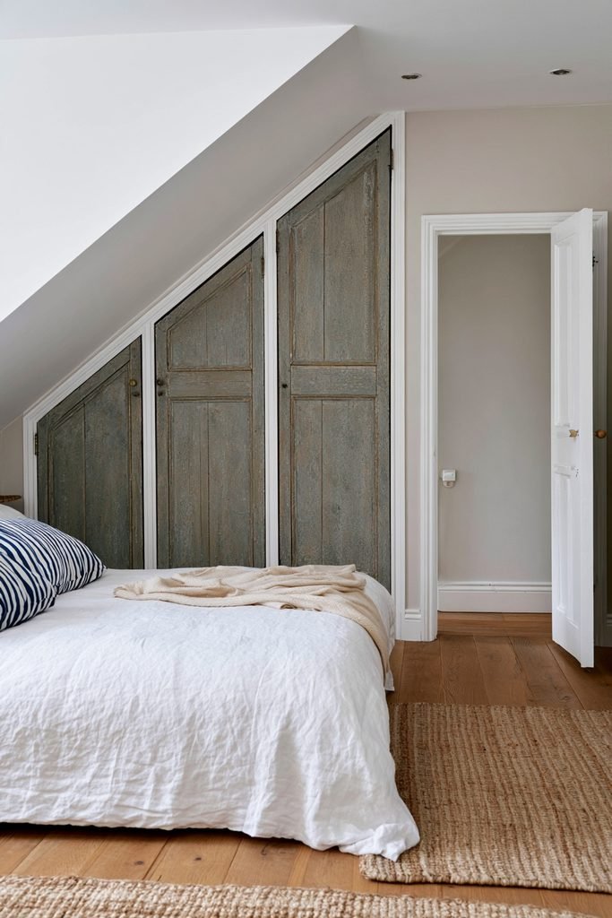 Compact loft bedroom with reclaimed timber wardrobe beneath a sloping roof, double bed, rooflight, and oak flooring