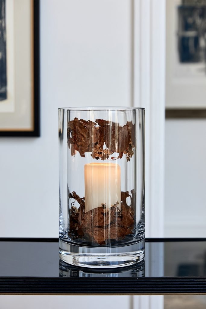 Double glass candle jars with suspended pressed autumn leaves and dried flowers in a modern fall home.