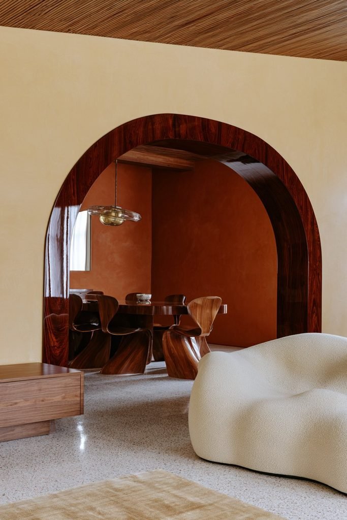 High-gloss cherry wood arched opening connecting a colorful mid-century living room and dining area.