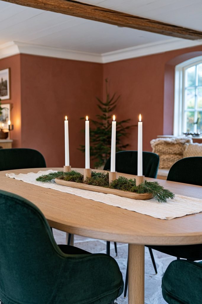 Four white Advent taper candles arranged in a wooden holder with pine sprigs and moss on a linen-covered Scandinavian Christmas dining table.