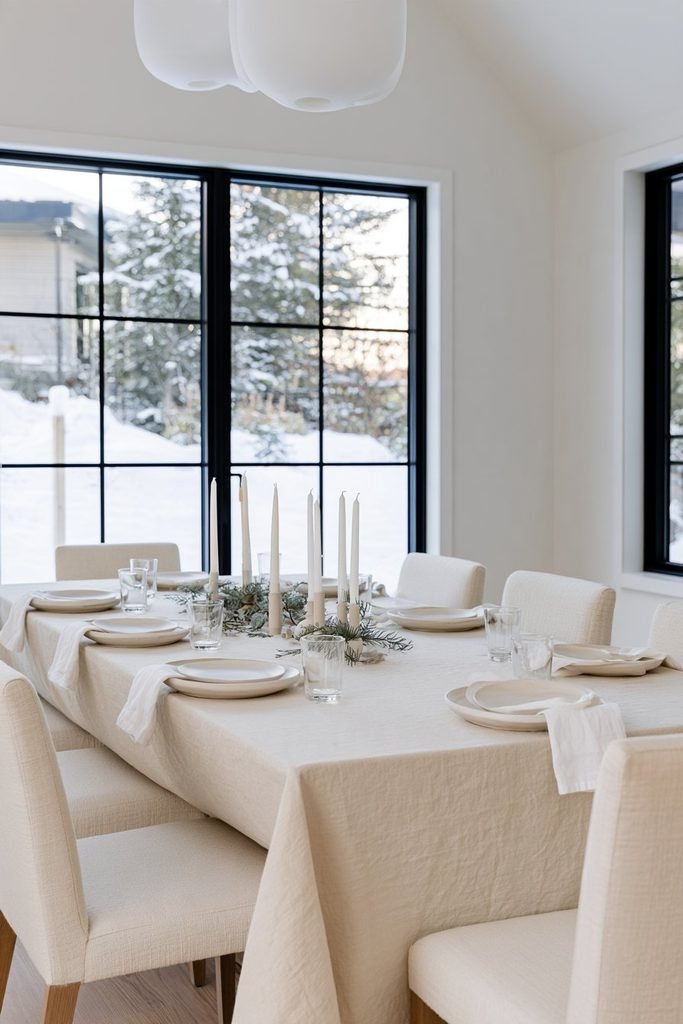 Elegant white Christmas dining table decor featuring a round marble pedestal table, white bouclé chairs, frosted greenery, and a cozy winter-inspired dining room.