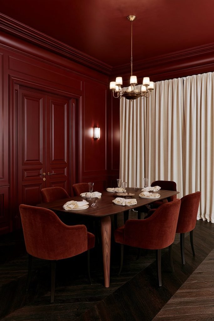 Burgundy colour-drenched dining room with matching walls, ceiling and trim, dark walnut table and brass chandelier