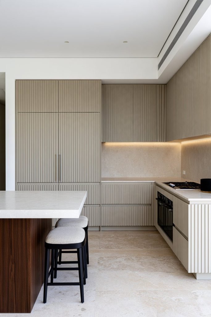 Contemporary kitchen with a floor-to-ceiling taupe fluted cabinetry wall concealing pantry and appliance doors, paired with a walnut kitchen island.