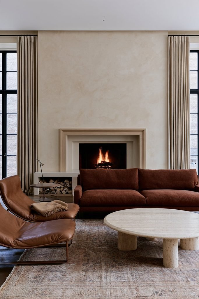 Burnished greige Venetian plaster fireplace wall with an oak mantel, leather sofa, and natural stone coffee table