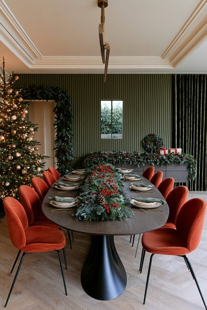 Christmas dining table decor featuring a lush evergreen garland runner, an oval smoked-oak table, black metal pedestal legs, and rust velvet dining chairs.