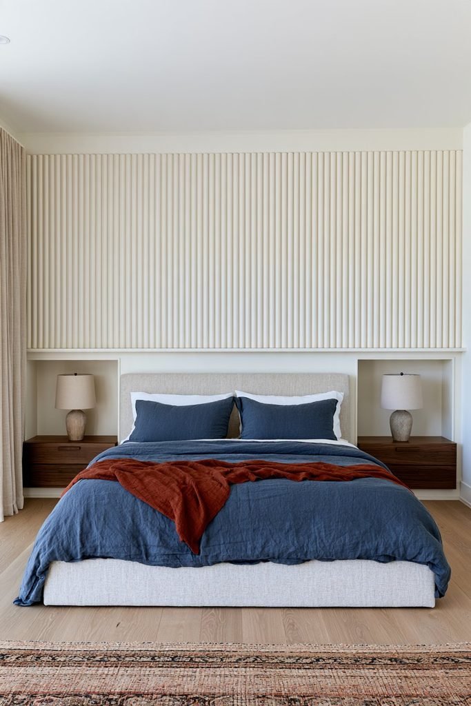 Cozy bedroom featuring a full-width half-round molding wall treatment painted warm cream, with an upholstered bed, bedside niches, and natural wood flooring.