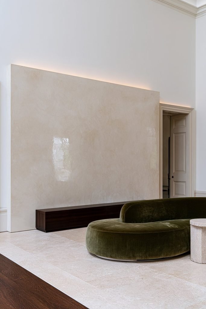 High-gloss burnished Venetian plaster wall with marble-like movement, walnut console, olive velvet seating, and limestone floor