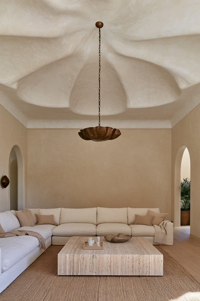 Hand-troweled plaster statement ceiling with organic texture and sculptural brass pendant in a warm living room