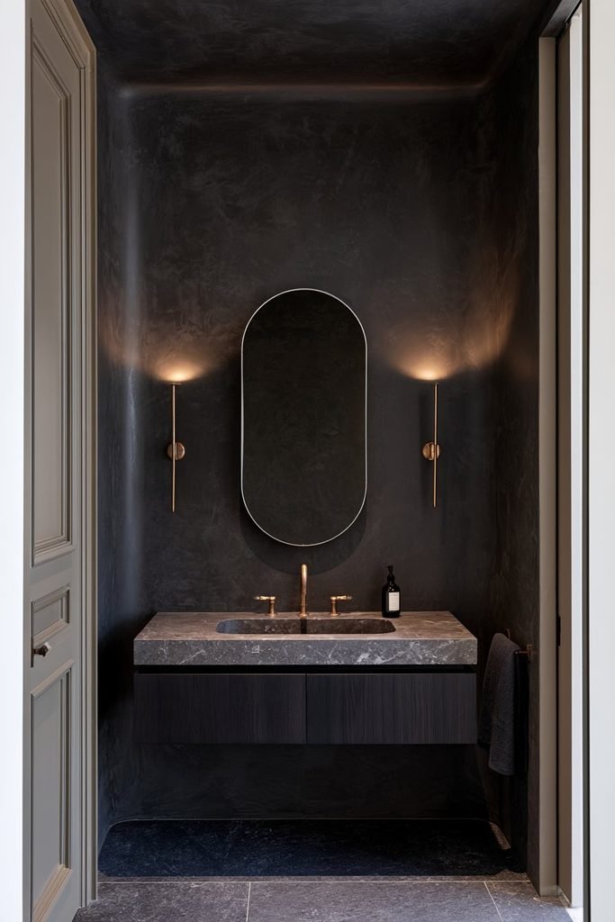Deep charcoal Venetian plaster walls and ceiling in a compact powder room with brass sconces and dark walnut vanity