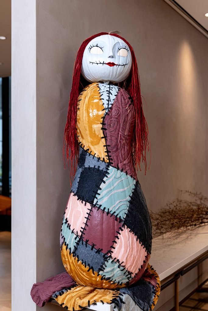 Sally dress-inspired pumpkin featuring colorful fabric-style patches and black stitching for a whimsical Nightmare Before Christmas decoration.