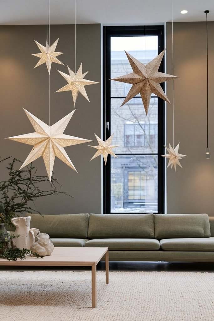 Handmade three-dimensional Scandinavian paper Christmas stars in cream and kraft paper hanging near a window in a minimalist living room.