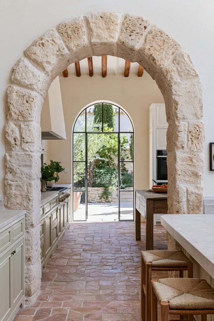 Natural travertine stone arched doorway leading from a Mediterranean kitchen to an outdoor courtyard.